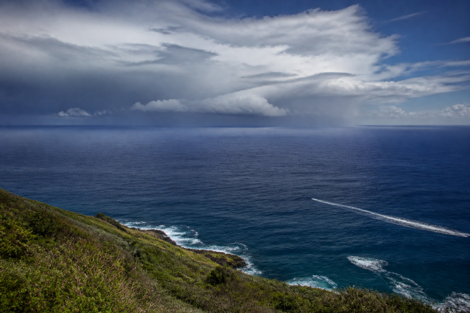 Deep blue Pacific Ocean beneath a distant band of tropical storm clouds