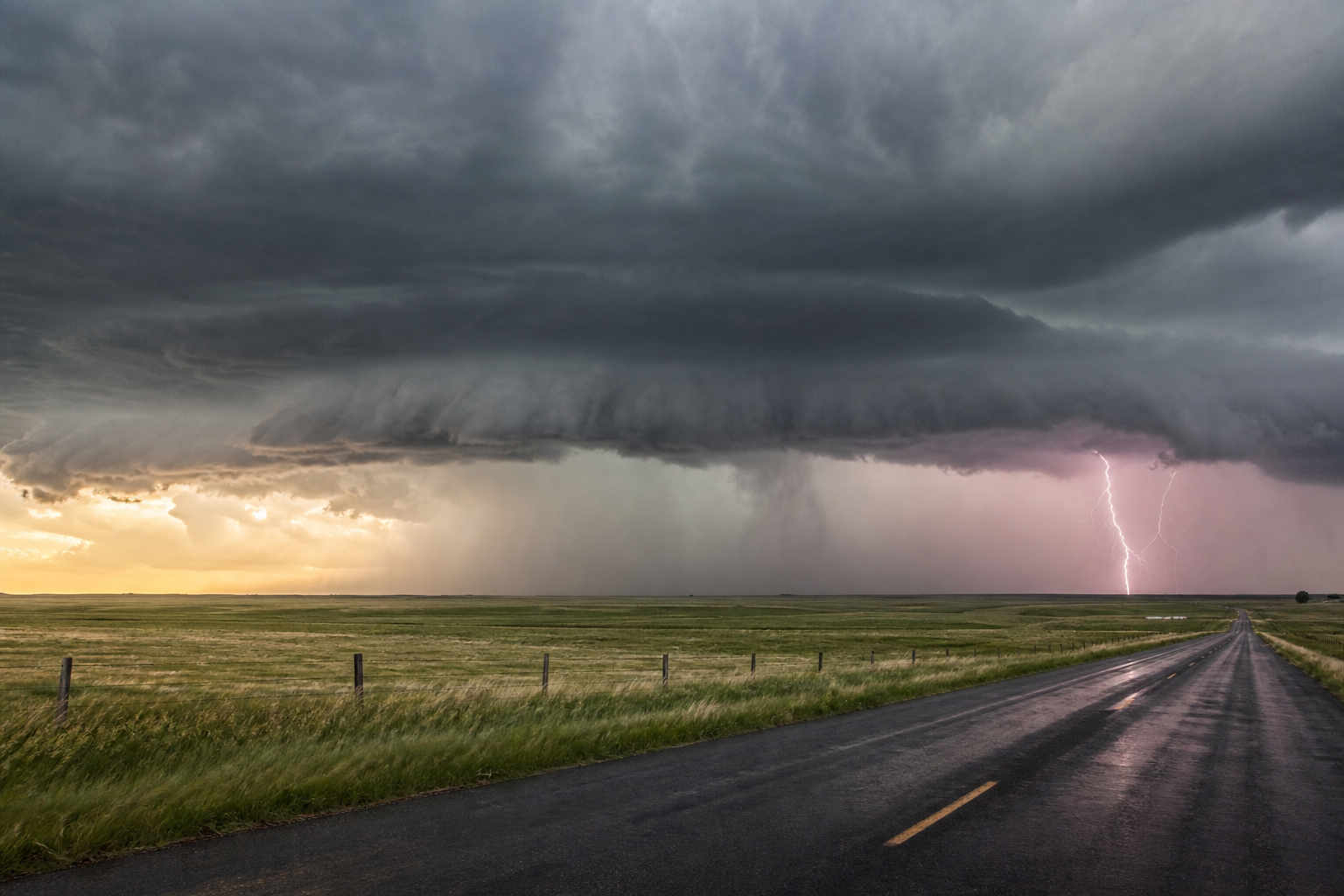 Dark severe thunderstorm clouds over open Plains farmland and a wet rural road